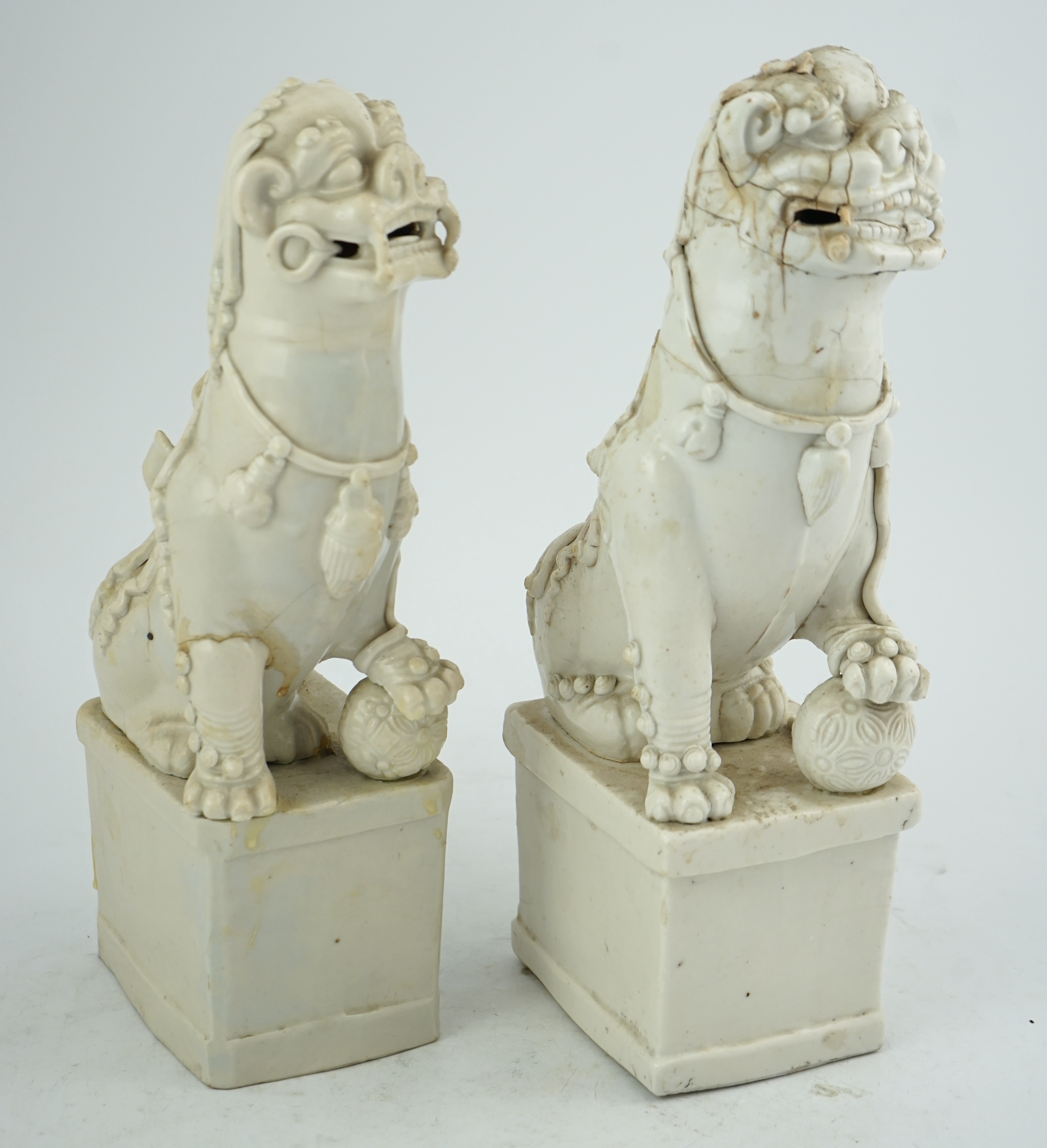 Two large Chinese Dehua blanc de chine Buddhist lion joss-stick holders, Kangxi period, each seated, one paw raised on a ball, on rectangular pedestal basis, 35cm high, Condition - extensive cracks or repairs